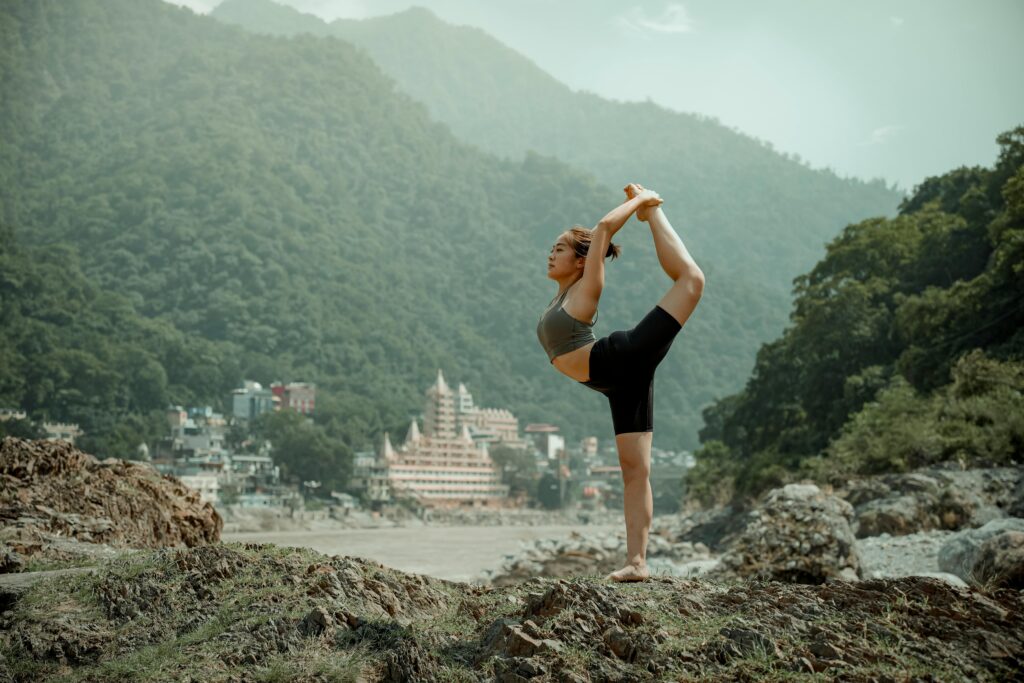 Young woman practicing yoga in Rishikesh with a backdrop of mountains and temples.