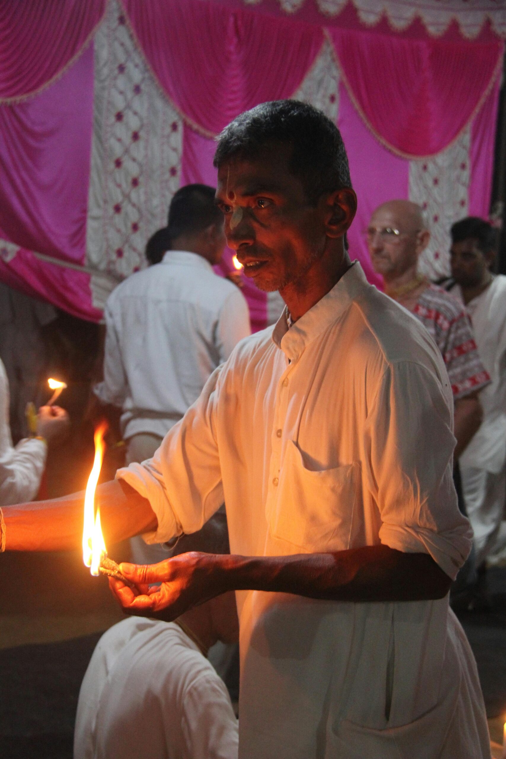 A man participates in a traditional candle ceremony indoors at Vrindavan, India.